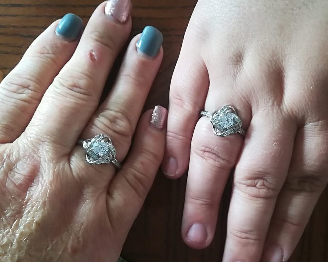 Two hands side by side on a wooden table, each wearing the same silver knot ring