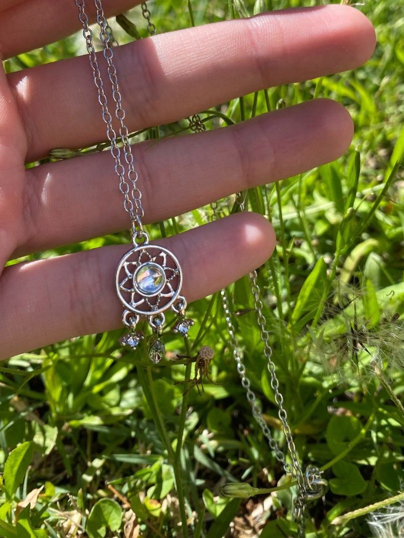 The dream catcher necklace held up over the grass