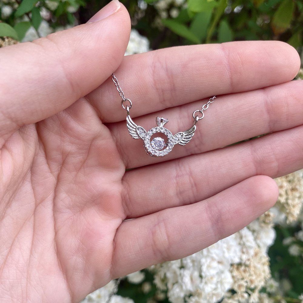 An angel wing necklace held out in an open palm